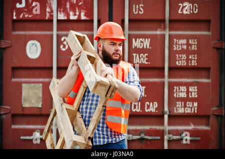 Brutal beard worker man suit construction worker in safety orange helmet with pallet. Stock Photo