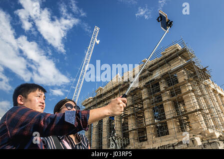 Asian tourists with selfie stick in front of Parthenon temple dedicated to the goddess Athena, part of Acropolis of Athens city, Greece Stock Photo