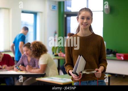 Teenage girl smiling for the camera during her design and technology lesson. She has some equipment in her hand and there are other students working i Stock Photo