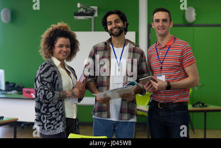 Three teachers standing together with paper work and a digital tablet. They are smiling and looking at the camera. Stock Photo