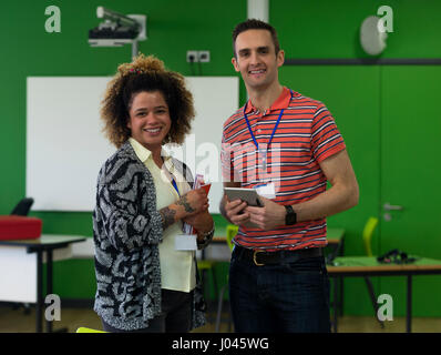 Two teachers standing together with paper work and a digital tablet. They are smiling and looking at the camera. Stock Photo