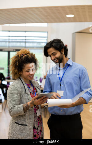 Two teachers are holding some paperwork and a digital tablet in front of them and are discussing it together. Stock Photo