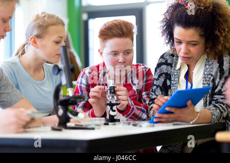 Students sitting with teacher in a lesson. They are using microscopes and a digital tablet. Stock Photo