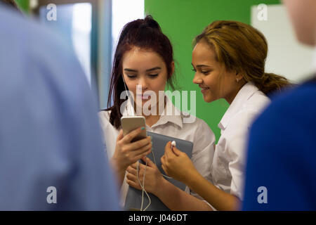 Two students sharing headphones which are connected to a smartphone. they are watching the screen of the phone and have a digital tablet with them. Stock Photo
