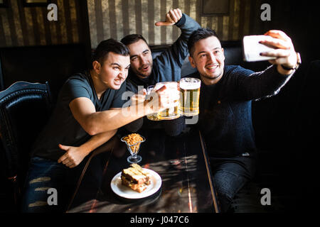 people, leisure, friendship, technology and party concept - happy male friends taking selfie and drinking beer at bar or pub Stock Photo