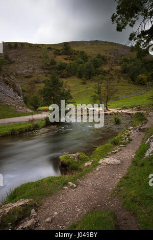 A view toward the stepping stones on the river Dove in Dovedale, Derbyshire. Slow shuuter speed blurs the water and several blury shaddows of people a Stock Photo