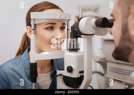 Doctors check up. Beautiful attractive pleasant woman resting her head on a special device and checking her eyesight while visiting an ophthalmologist Stock Photo