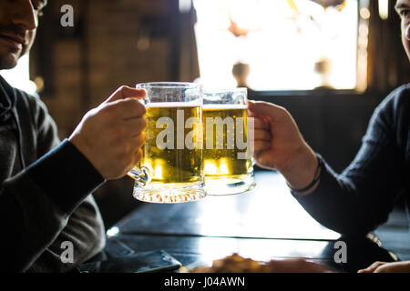 people, leisure and drinks concept - close up of male hands clinking beer glasses and pretzels at bar or pub Stock Photo