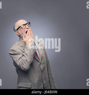 Yawning senior man in suit on gray background with copy space