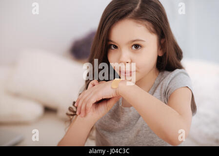 Little girl putting adhesive bandage on her injury at home Stock Photo
