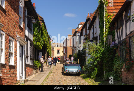 Rye, England, UK - June 8, 2013: Pedestrians and tourists walk past traditional brick and tile cottages on a cobbled street in the picture postcard to Stock Photo