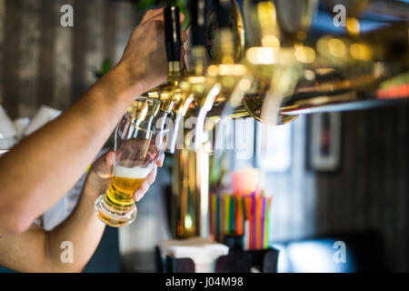 barman hand at beer tap pouring draught lager beer serving in a restaurant or pub. Stock Photo