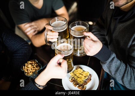 people, leisure and drinks concept - close up of male hands clinking beer glasses and pretzels at bar or pub Stock Photo