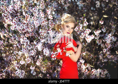 https://l450v.alamy.com/450v/j04ttt/beautiful-young-woman-in-nice-red-dress-posing-on-flowering-trees-j04ttt.jpg