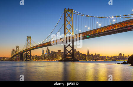Classic panoramic view of famous Oakland Bay Bridge with the skyline of San Francisco illuminated in beautiful twilight after sunset, California, USA Stock Photo