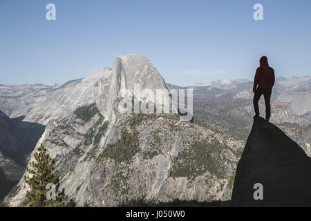 A young hiker is standing on a rock enjoying the view towards famous Half Dome at Glacier Point at sunset, Yosemite National Park, California, USA Stock Photo
