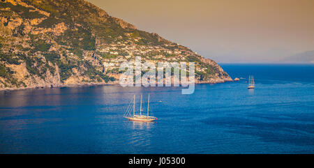 Panorama view of sailing yachts on the Mediterranean Sea at famous Amalfi Coast in beautiful golden evening light at sunset in summer, Positano, Italy Stock Photo