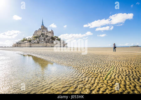 Panoramic view of famous historic Le Mont Saint-Michel tidal island with male tourist taking a photograph on a sunny day in summer, Normandy, France