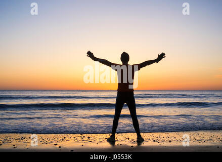 Jogger stretching on beach at sunrise. UK Stock Photo