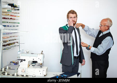 Young businessman speaking on cellphone while visiting tailor Stock Photo