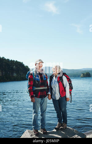 Active pensioners with backpacks looking at camera with lake on background Stock Photo
