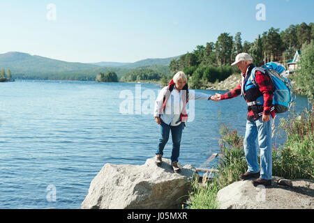 Mature man helping his wife walk on stone during trip in the country Stock Photo