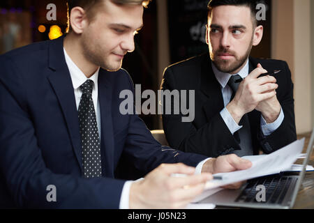 Portrait of two successful business partners working during meeting: reading documents and discussing deal Stock Photo