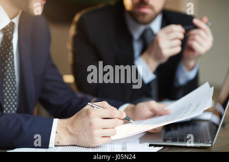 Closeup portrait of two unrecognizable  business partners reviewing paperwork and signing contract papers at table during meeting Stock Photo