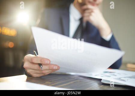 Closeup portrait of unrecognizable successful businessman wearing black formal suit analyzing documents and finance statistics at desk, thinking Stock Photo