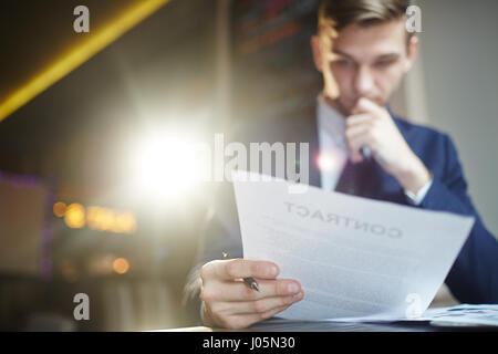 Portrait of young successful businessman reading contract documents at desk, busy with paperwork, focused Stock Photo