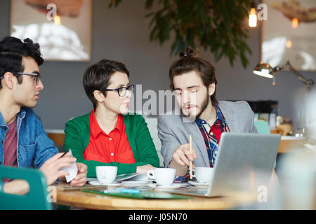 Group of young creative people collaborating at meeting in cafe, discussing work Stock Photo