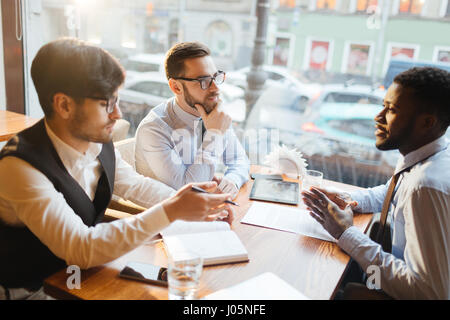 Three young men having start-up meeting in cafe Stock Photo