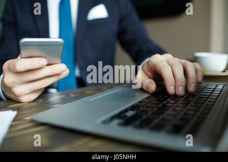 Closeup portrait of elegant businessman working with laptop and holding smartphone while browsing internet Stock Photo