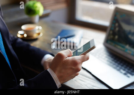 Closeup of unrecognizable elegant businessman using  smartphone typing text messages while working in cafe Stock Photo