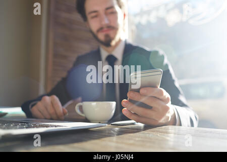 Portrait of handsome business man holding mobile phone bright sunlight with lens flare while working at table in office Stock Photo