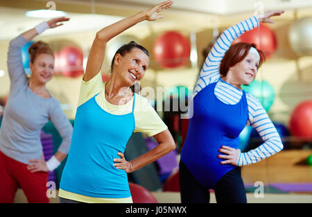 Aged women doing side-bends in gym Stock Photo