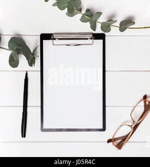 Mock-up with clipboard, pen and eucalyptus brunches on the white table Stock Photo