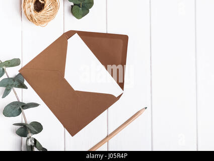 Blank envelope, pencil and eucalyptus brunches on the white table, top view Stock Photo