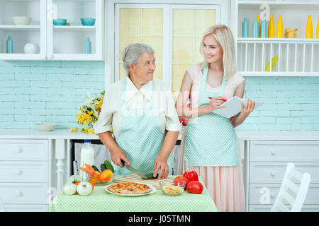 Grandmother tells cooking recipes of the young woman. She is learning to cook in the kitchen. Stock Photo