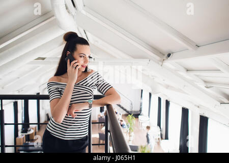 Portrait of a woman in a cafe leaning against the railing and talking on her phone. Stock Photo