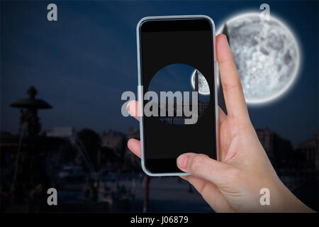 Human hand holding mobile phone against white background against large moon over city Stock Photo