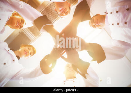 Chefs joining hands in a circle wearing uniforms in a kitchen Stock Photo
