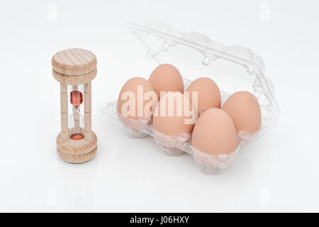 Wooden egg timer with box of eggs - as metaphor for that age-old question of which came first - chicken or egg. Stock Photo