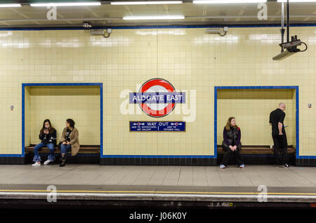 Passengers sit on benches in Aldgate East London Underground station as they wait on the platform for a train. Stock Photo