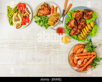 Dinner table with variety food, fried chicken wings, sausages, grilled vegetables in a pan, salad and  lager beer on wooden table. Top view. Copy spac Stock Photo
