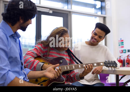 Music teacher helping students learn to play guitar. Stock Photo