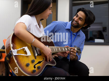 Music teacher helping a student learn to play guitar. Stock Photo