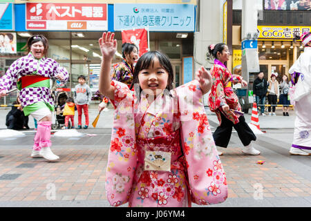 Japan, Kumamoto, Yosakoi dance festival. Close-up. Little smiling girl in pink kimono dancing in shopping mall with dance team behind her. Eye-contact