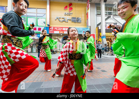 Japan, Kumamoto, Yosakoi dance festival. Dance team in colourful yukata, 2 men on either side, young teenage girl dances in middle, eye-contact.