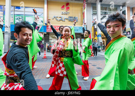 Japan, Kumamoto, Yosakoi dance festival. Dance team in colourful yukata, 2 men on either side, young teenage girl dances in middle, eye-contact.